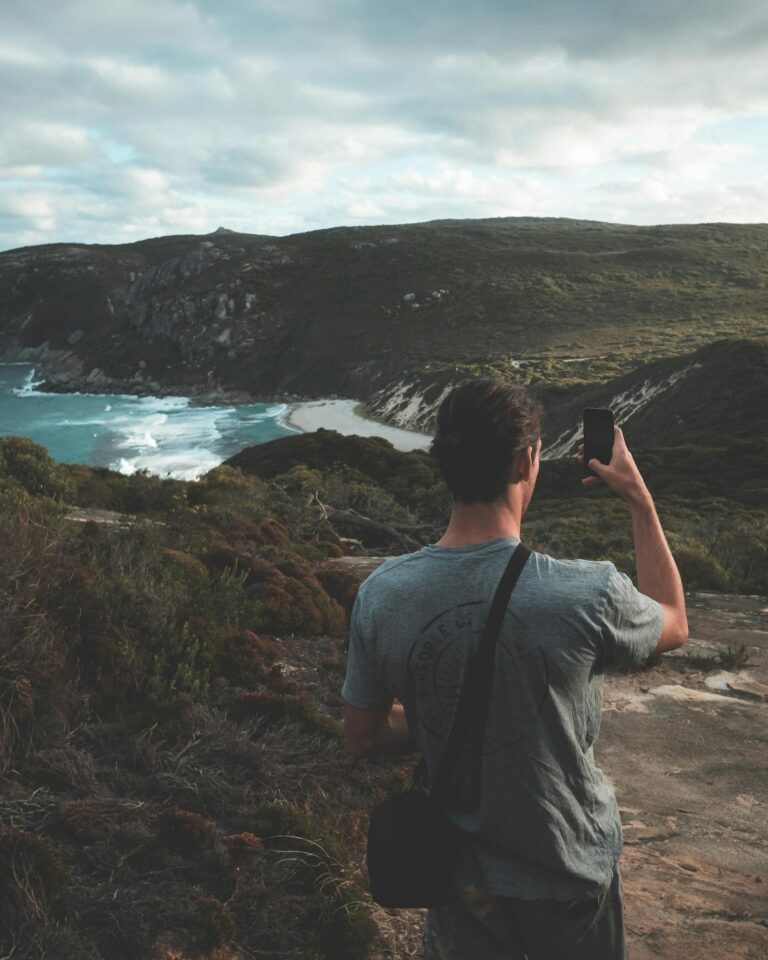 Anonymous hiker photographing sea and mountains against cloudy sky